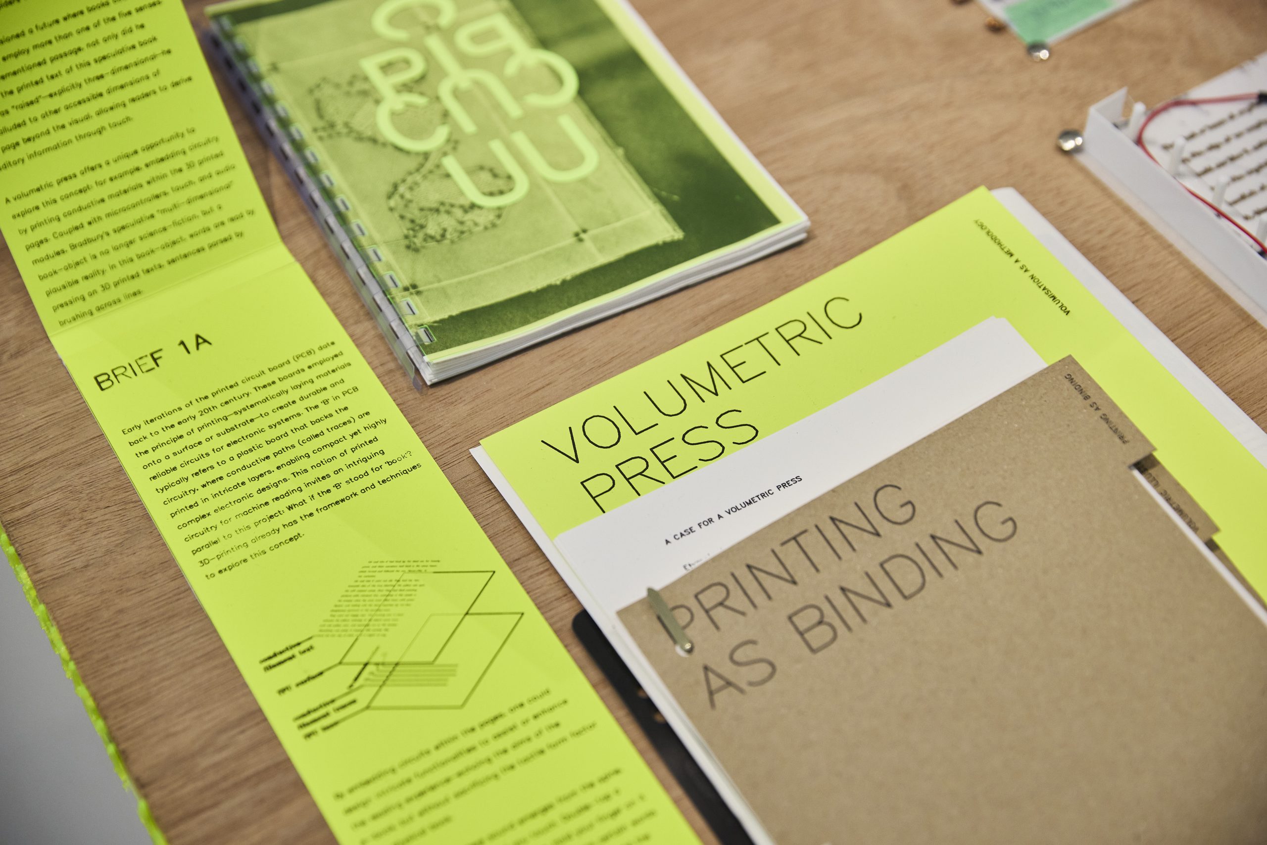 Close-up of a design project display with neon green and kraft paper prints featuring typographic layouts and publication titles.