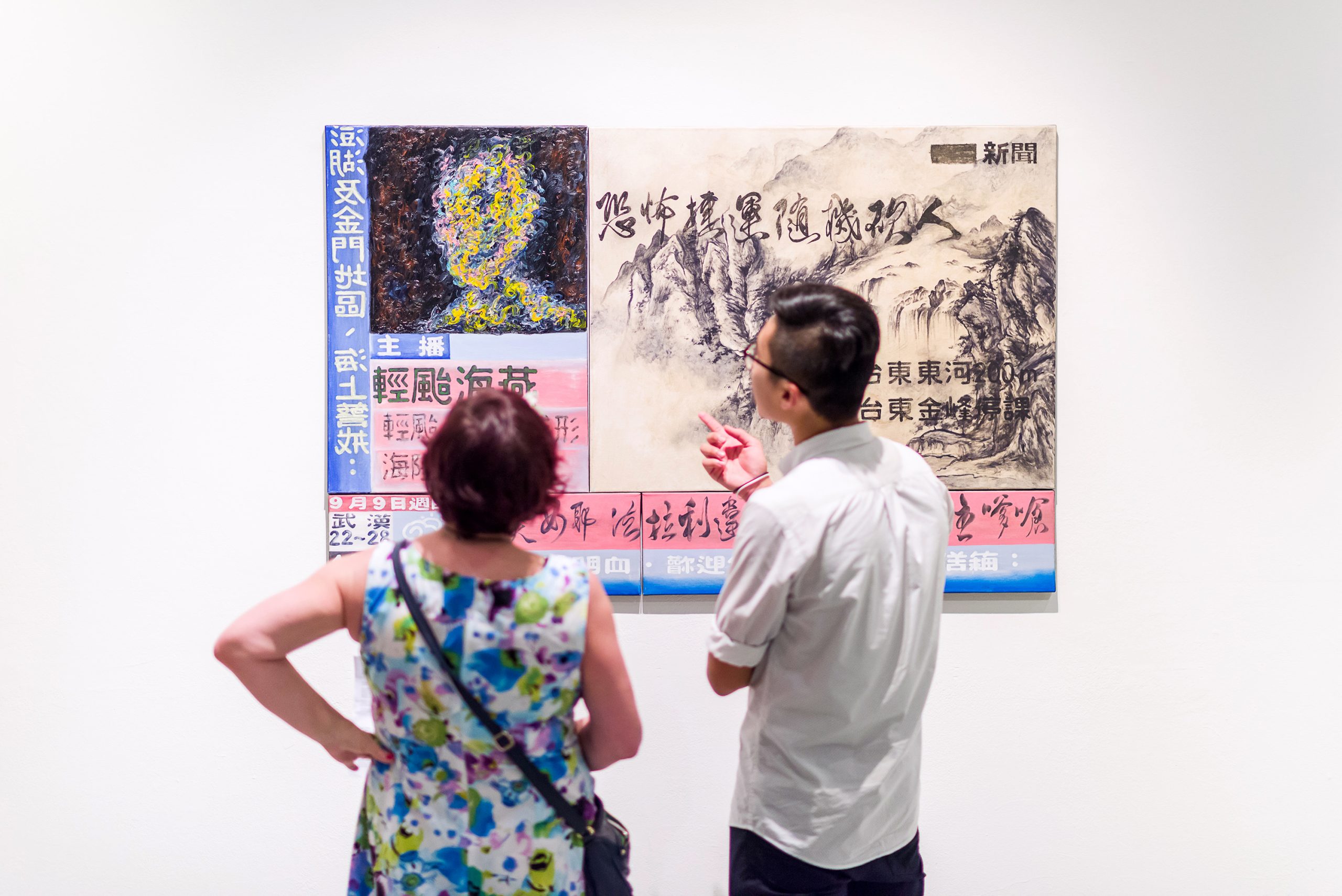 Two visitors discuss a mixed-media artwork of Chinese calligraphy, landscape illustration and painted textures on a white gallery wall.