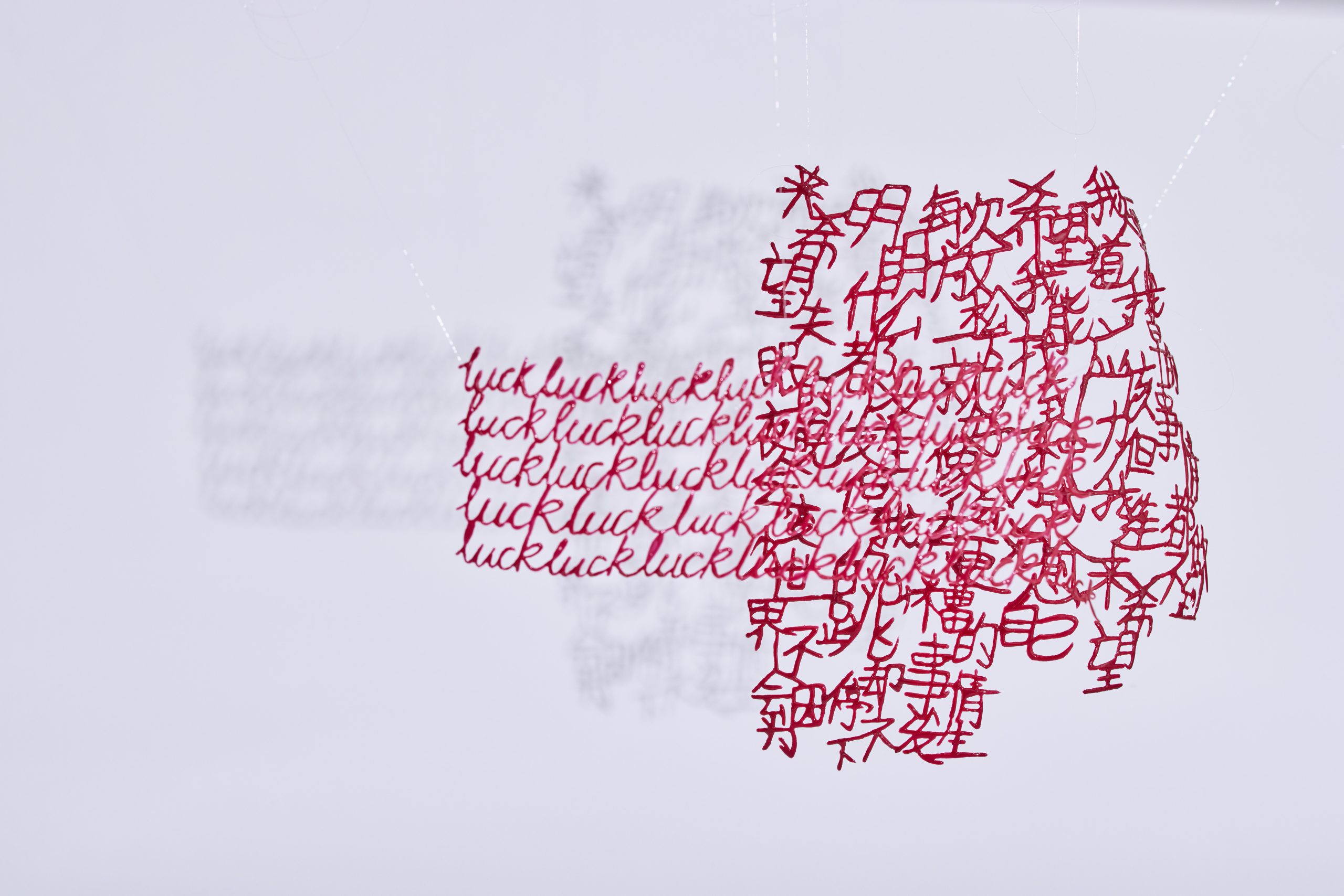 Suspended paper sculpture with layered red laser-cut Chinese characters and handwritten “luck” text, casting shadows on a white wall.