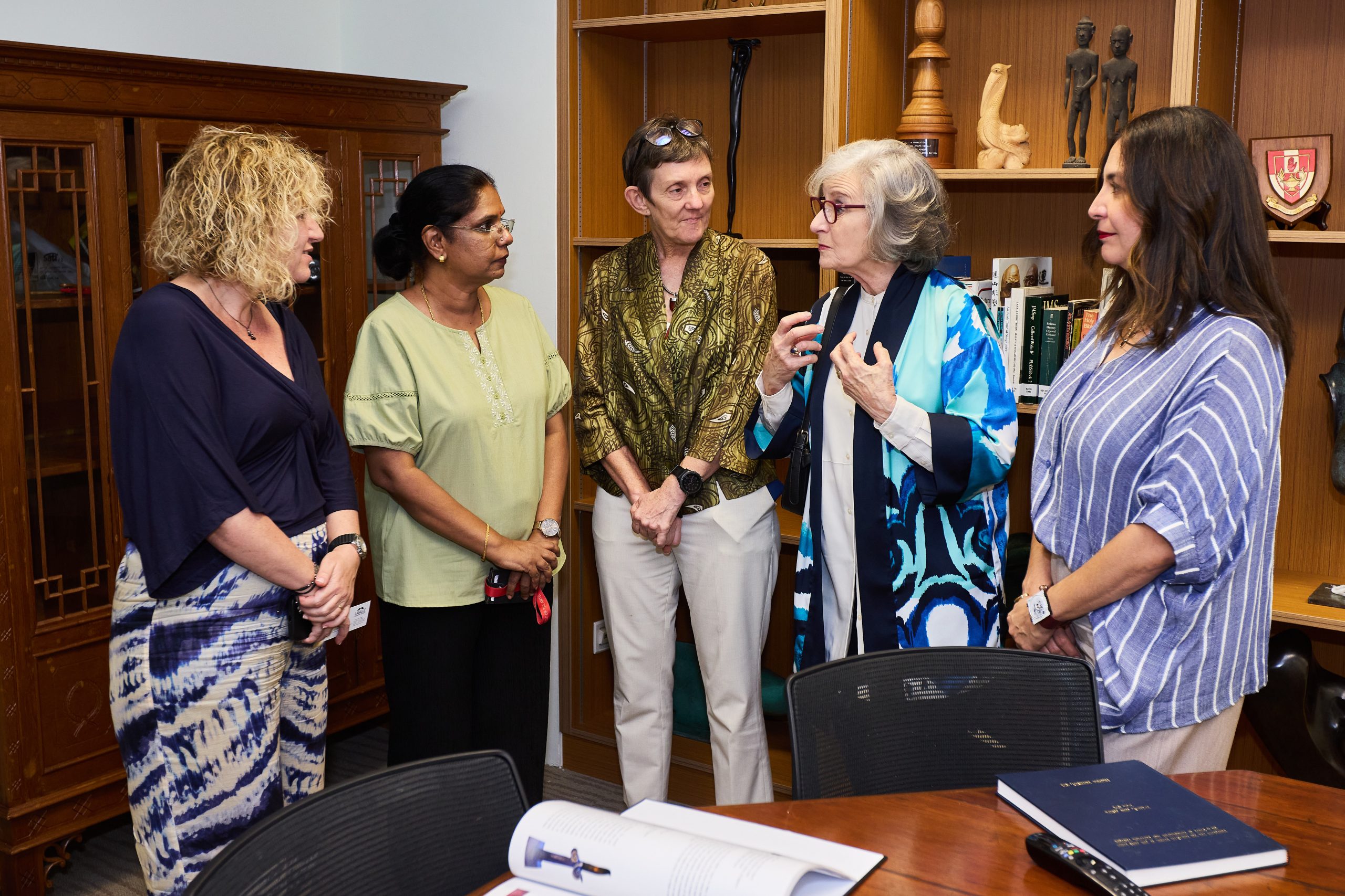 Group of LASALLE academic leaders and guests in conversation during an office visit, with books and documents on the table in the foreground.