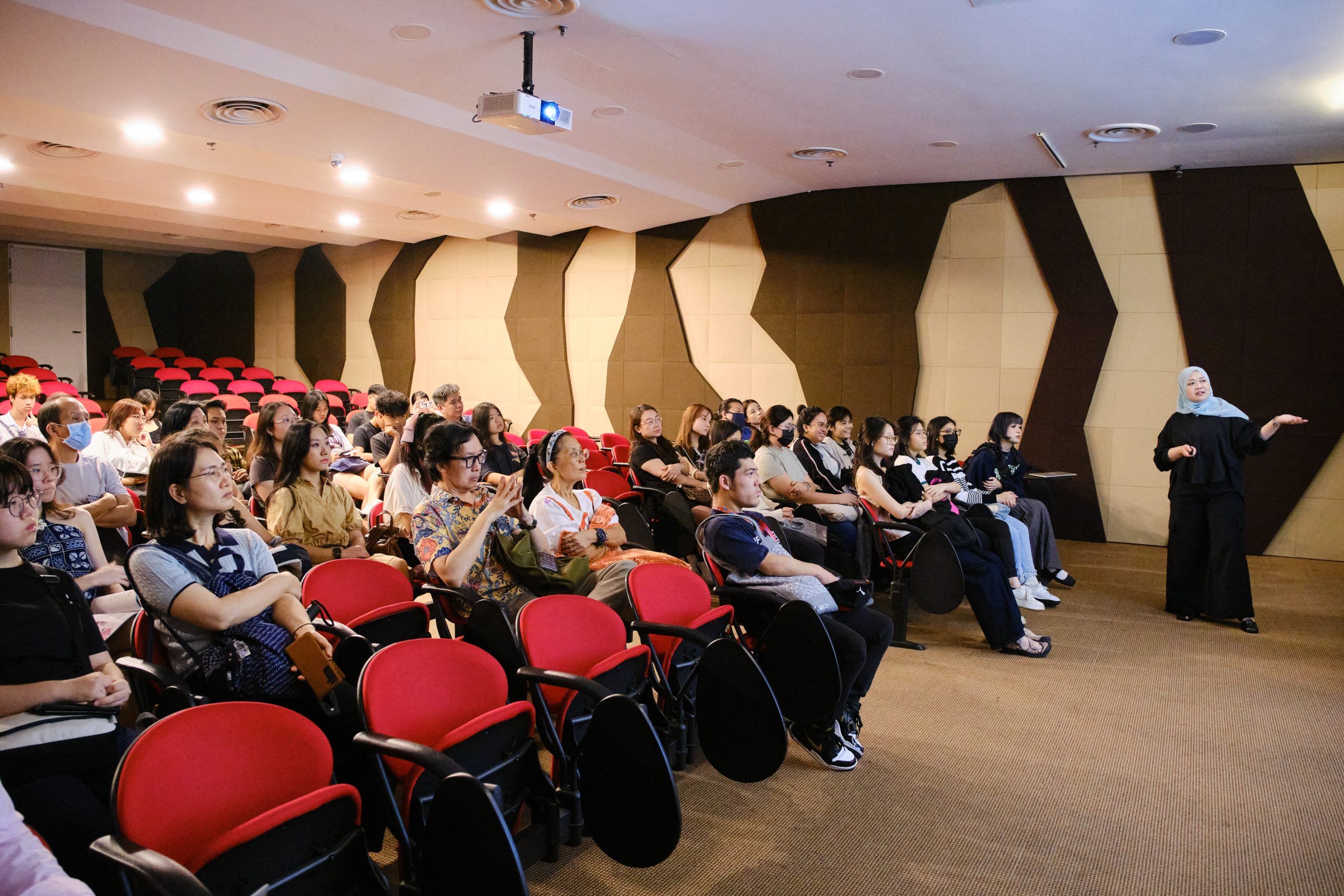 An audience of students and visitors listens attentively during a presentation in a tiered lecture theatre at LASALLE.