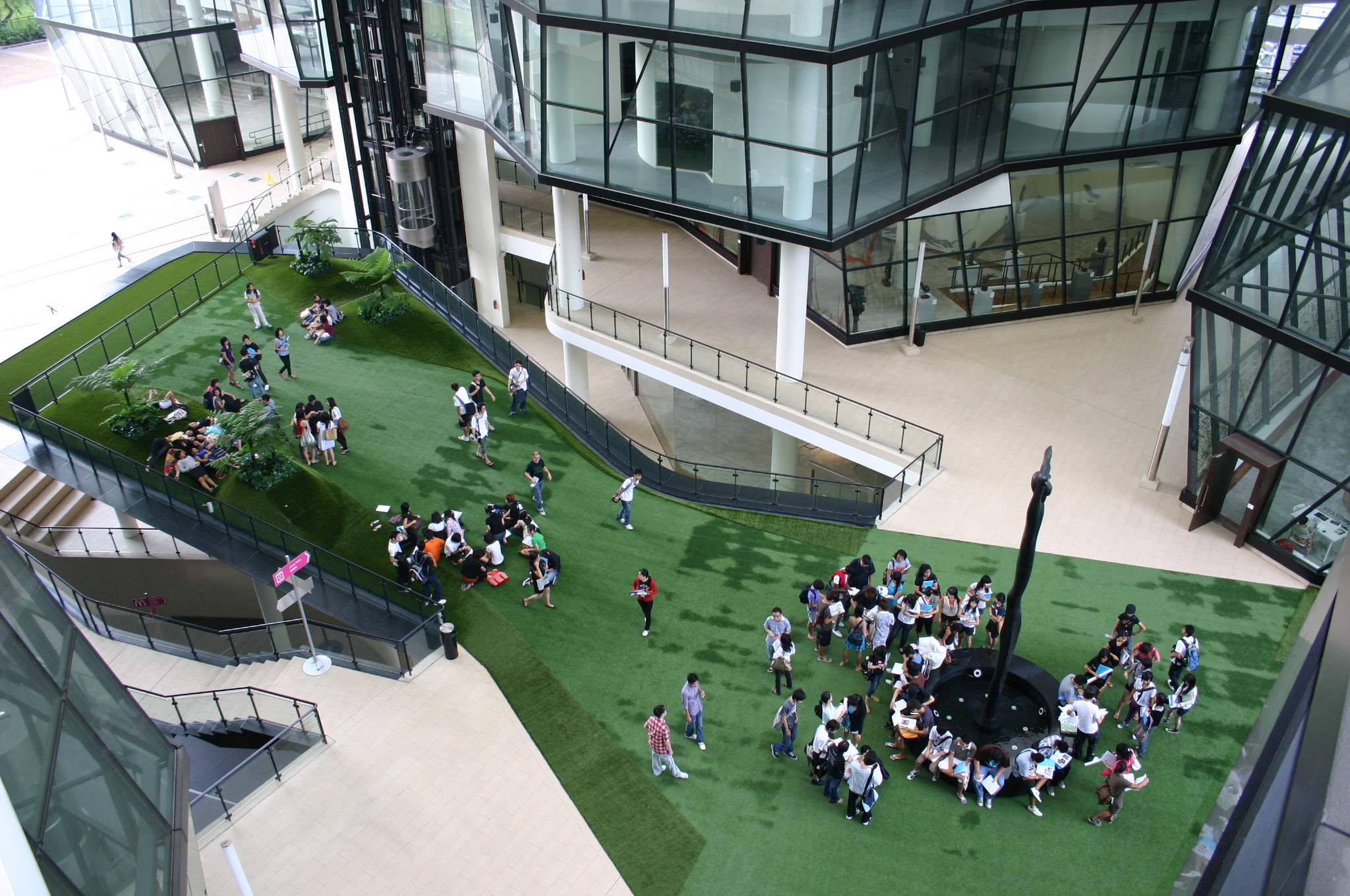Students gather in small groups across LASALLE’s green campus courtyard, framed by angular glass façades.