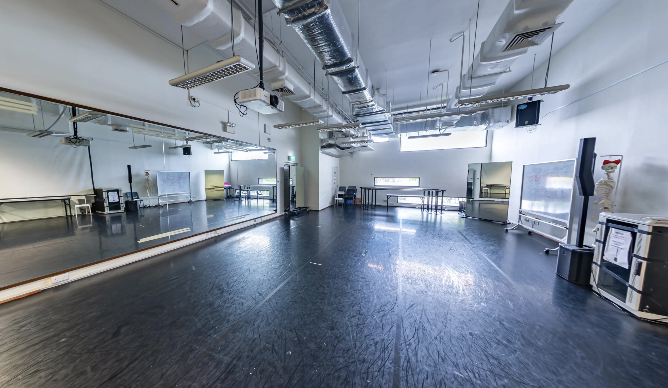 Spacious studio with full-length mirrors, black sprung flooring, AV equipment and anatomical skeleton model.