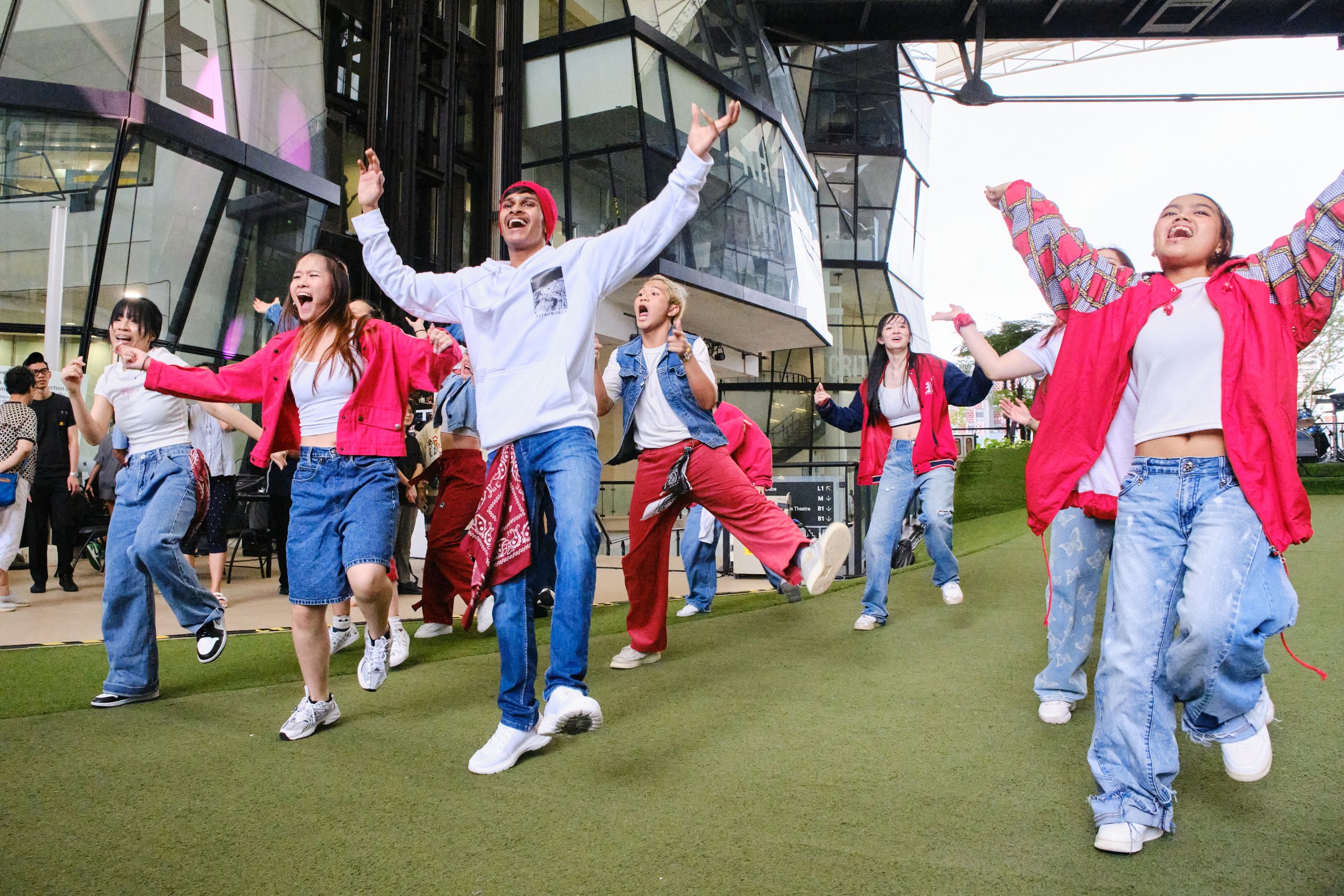 Group of LASALLE students in coordinated red and white outfits dancing energetically on the McNally Campus green during an outdoor performance.