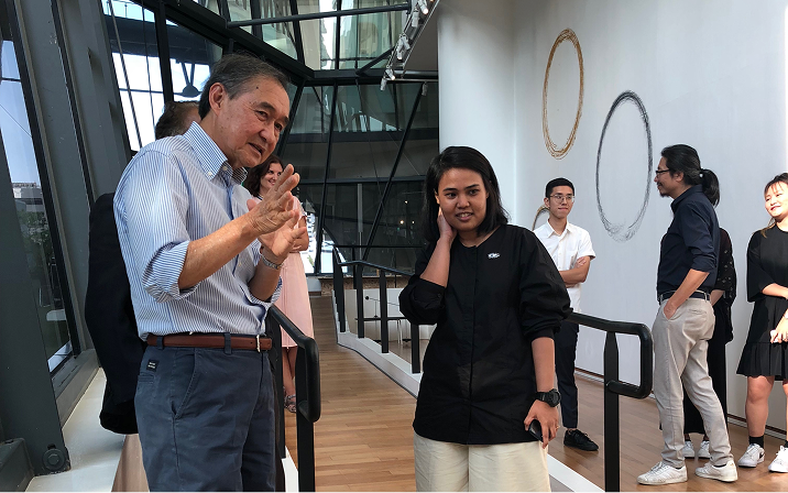 A man gestures while speaking with a woman at a LASALLE gallery, with other visitors chatting near wall art and glass windows.
