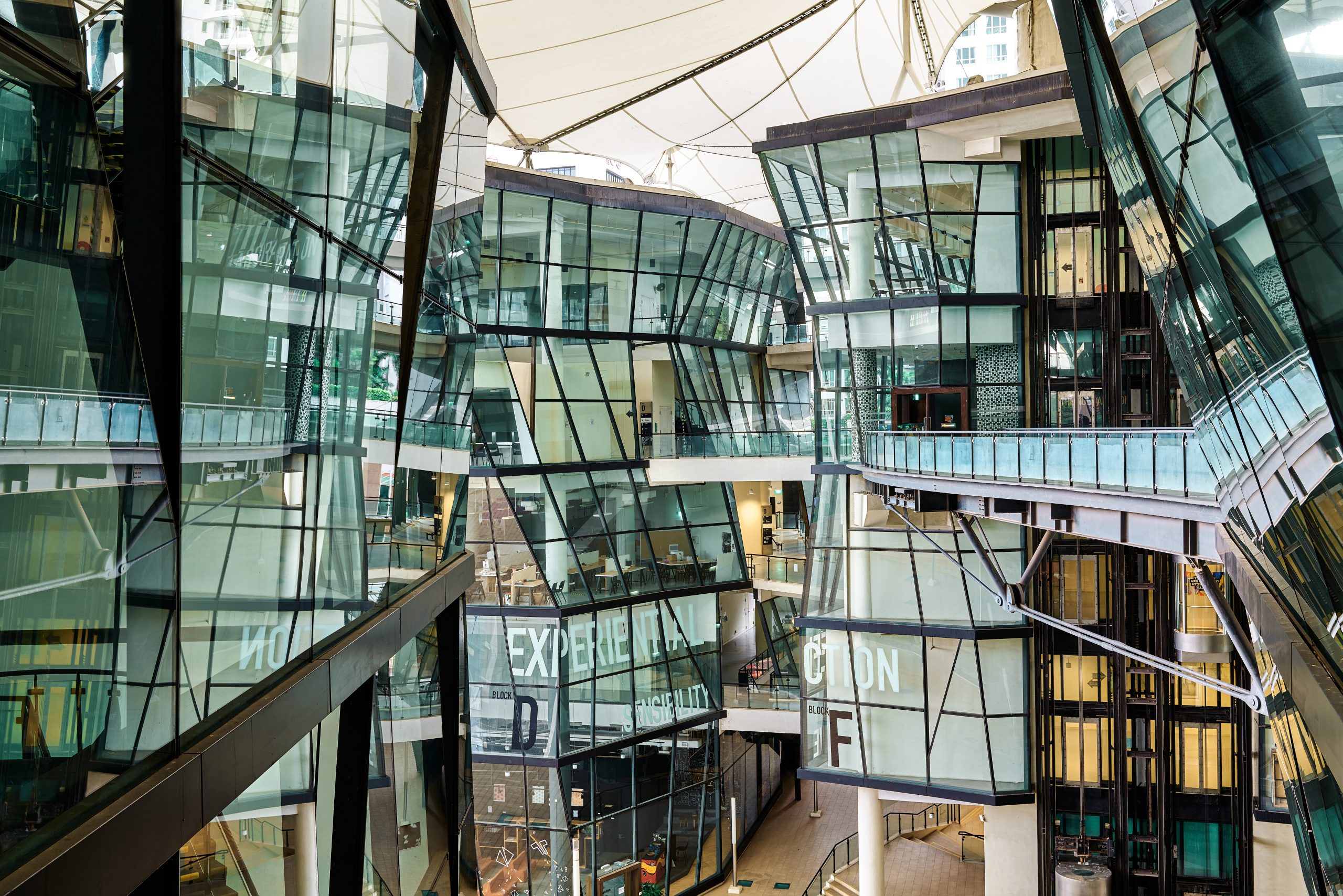Interior view of LASALLE’s McNally Campus, showcasing angular glass façades, floating walkways and open studio spaces under a tensile roof.