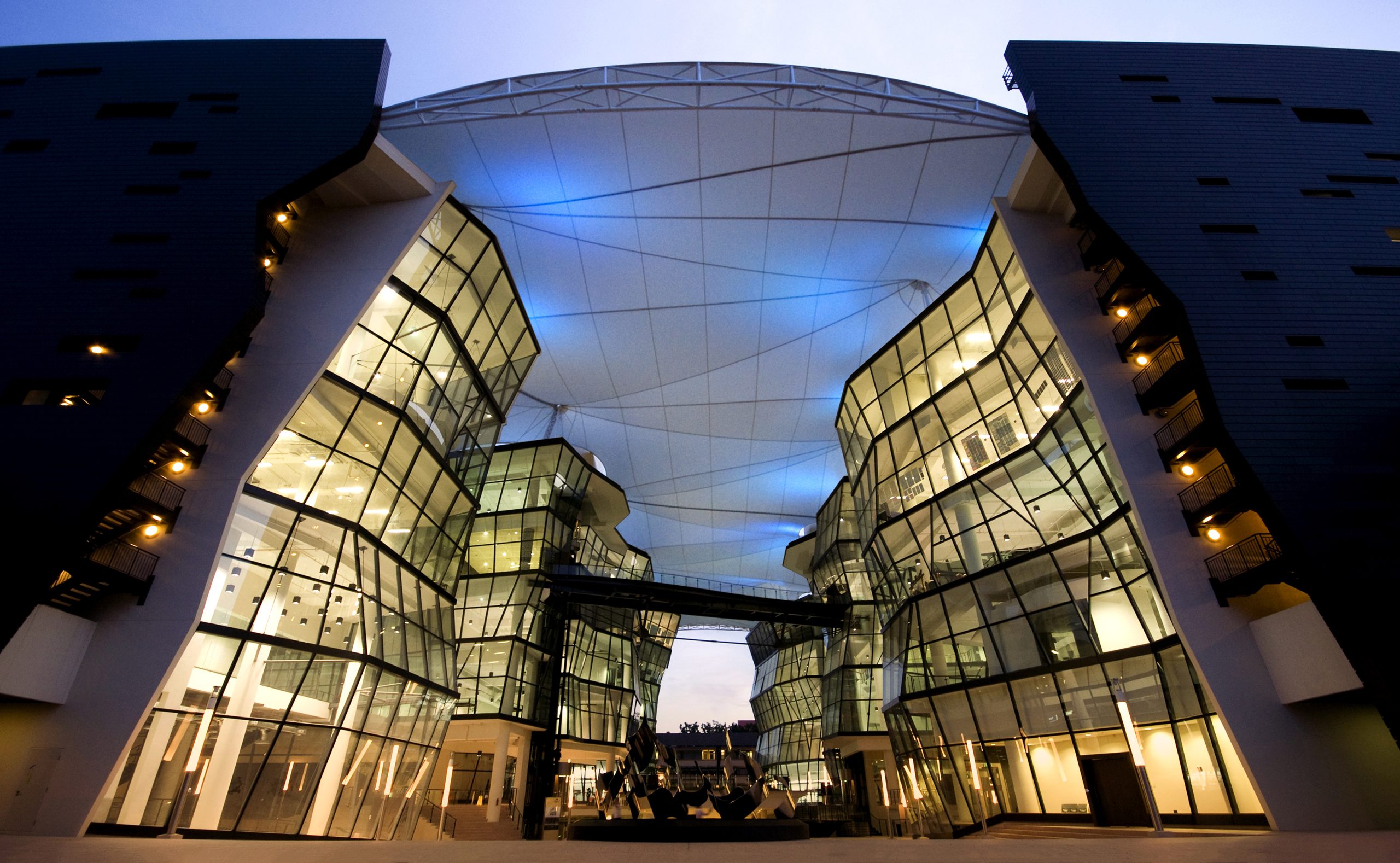Night view of LASALLE’s iconic glass buildings and roof canopy, dramatically lit with blue and warm lights.