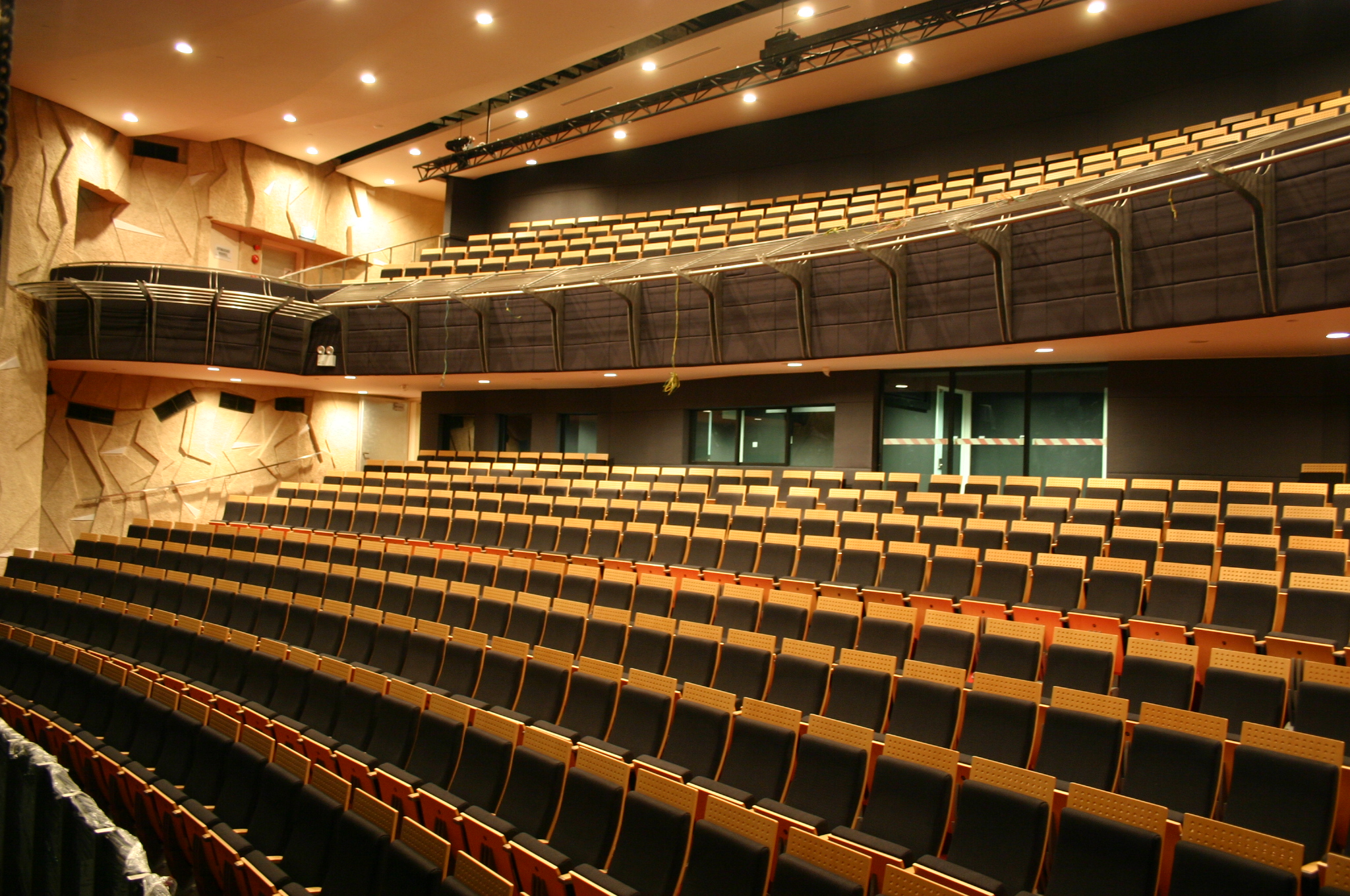 Interior of tiered theatre with warm lighting, textured acoustic walls and rows of empty black and wood-trimmed seats.