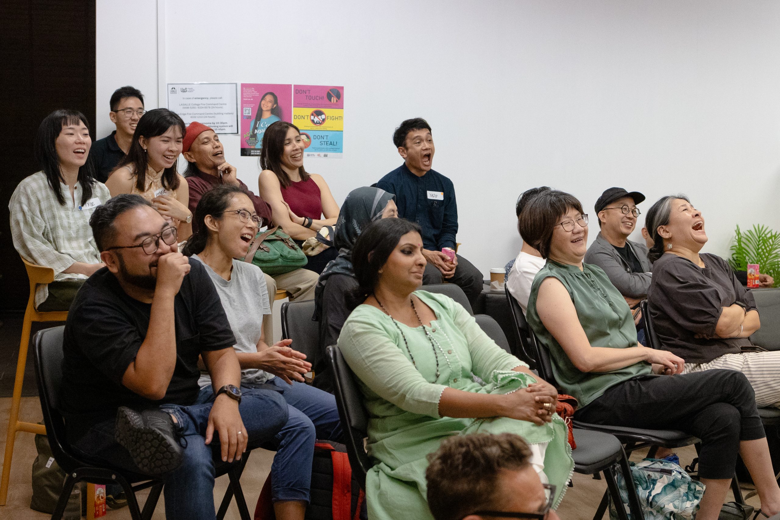 Audience members at a LASALLE event laugh and react with joy, seated closely together in an intimate classroom setting.