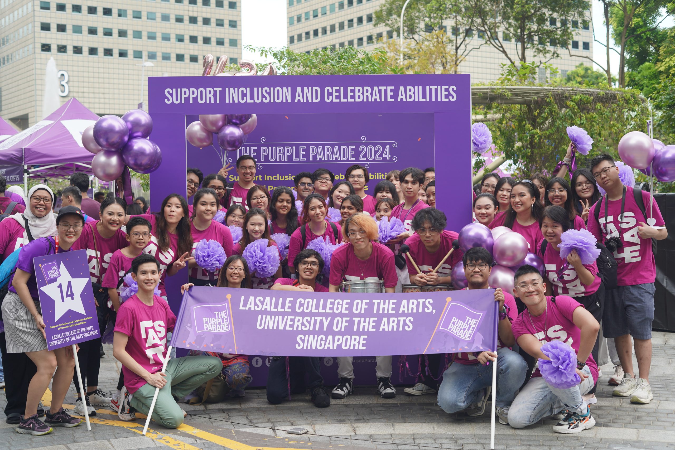 LASALLE students at The Purple Parade 2024 holding banners and pompoms, gathered under a sign promoting inclusion and abilities.