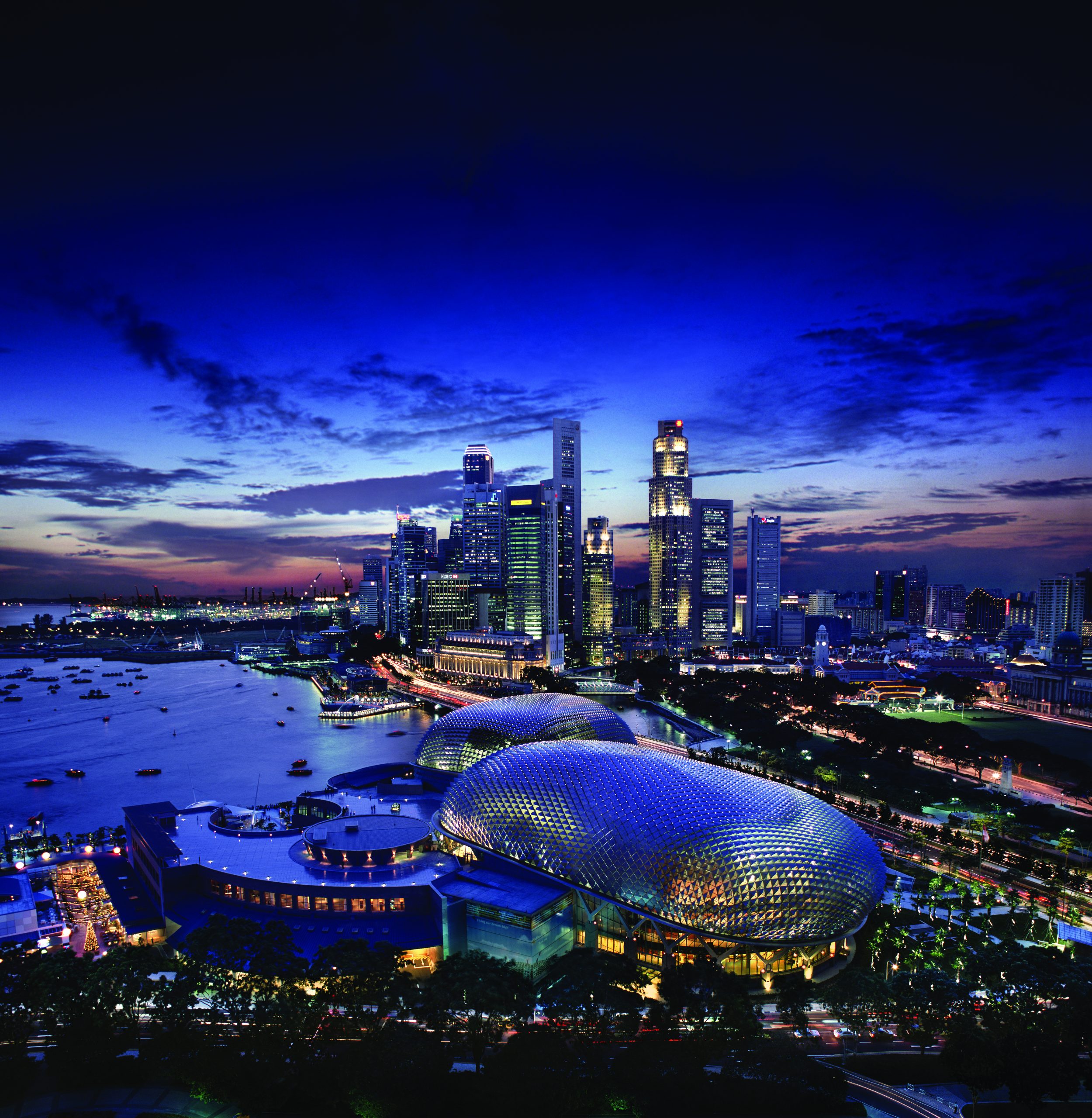 Aerial view of Singapore’s Marina Bay skyline at dusk, with skyscrapers lit against a deep blue sky and the Esplanade domes visible in the foreground.