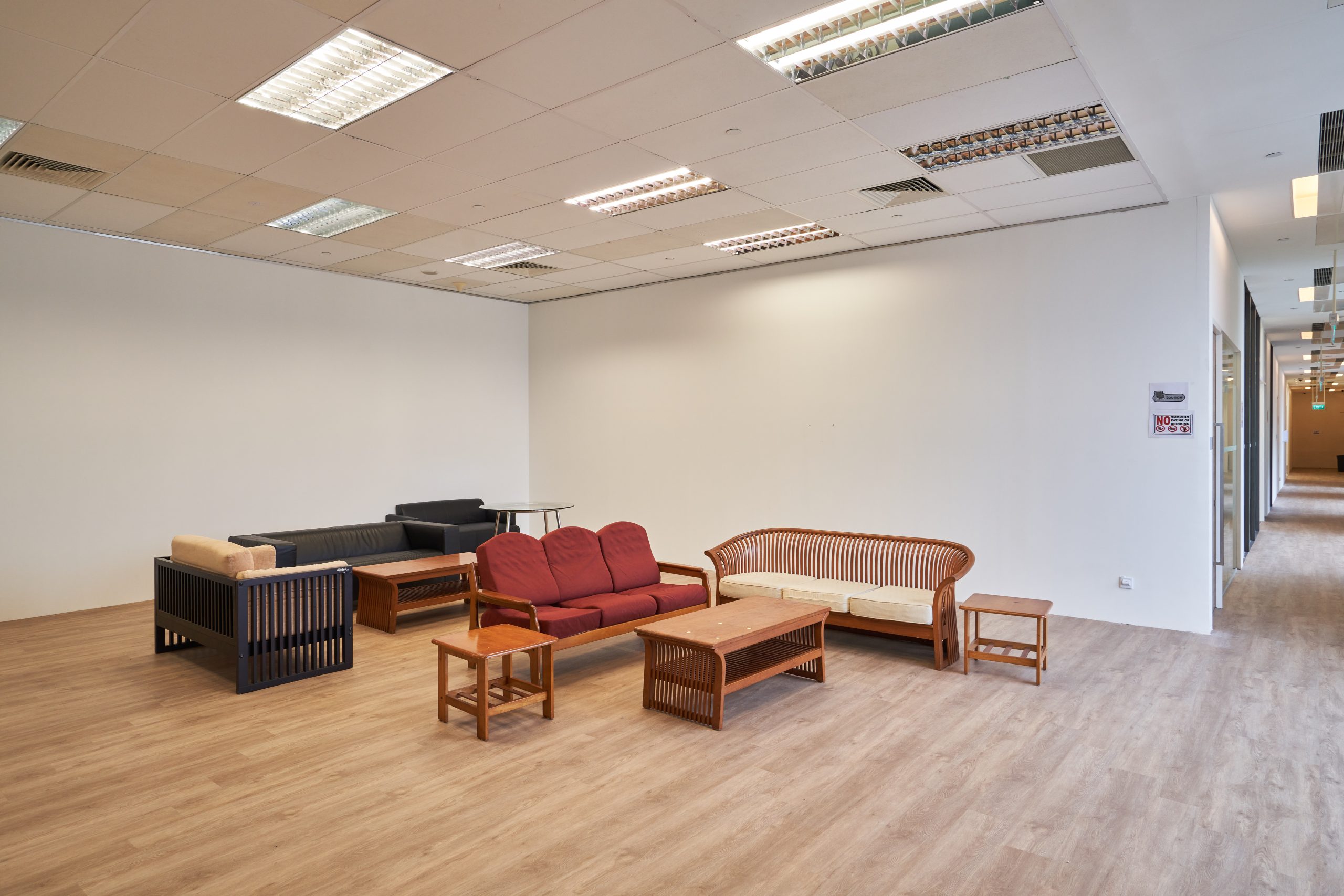 Assortment of sofas and wooden tables arranged in an open lounge space with wood flooring and white walls.