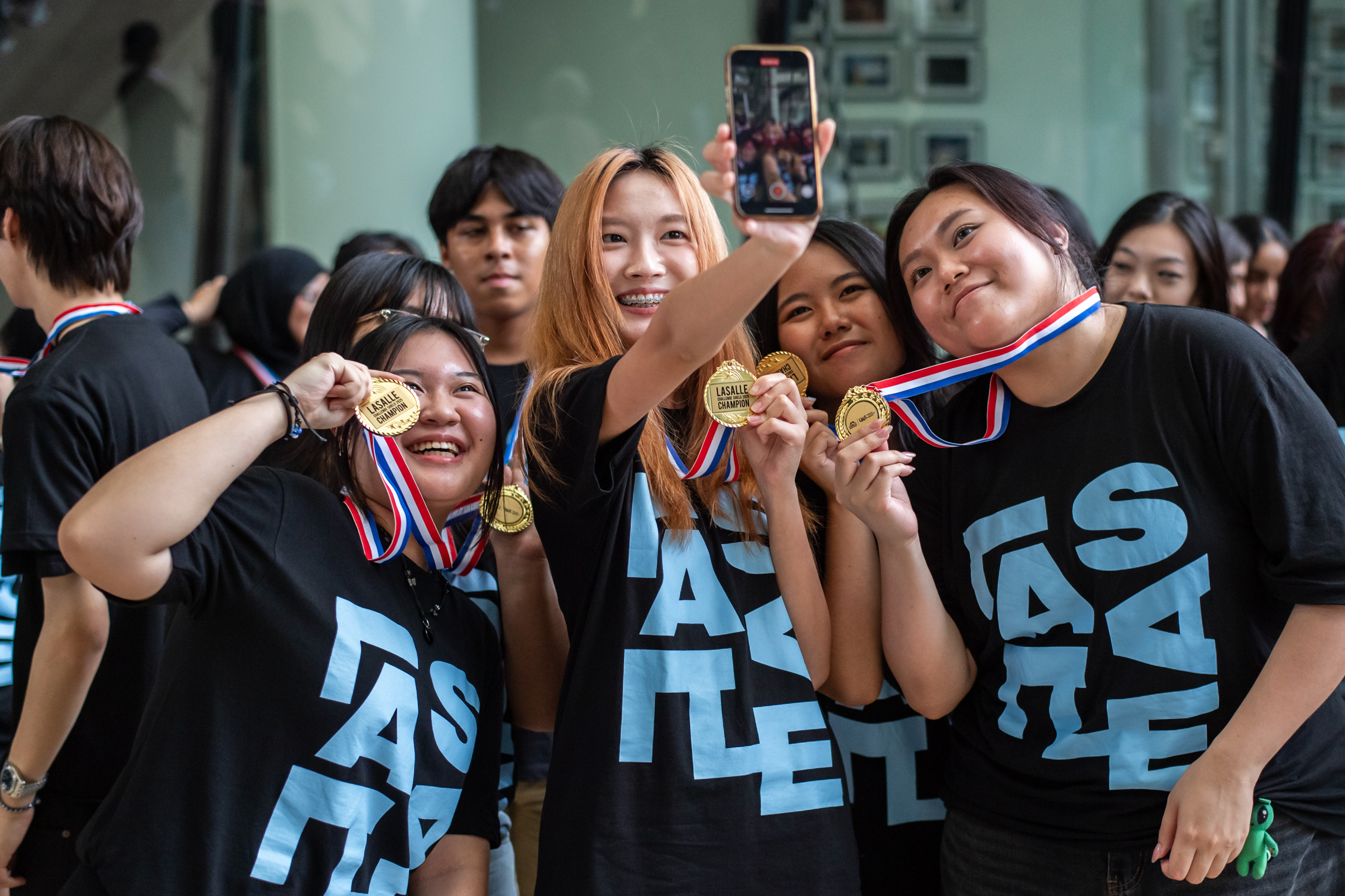 A group of students in t-shirts proudly displaying their medals, celebrating a recent achievement together.